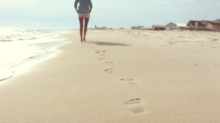 a woman walks on the beach, leaving footsteps in the sand