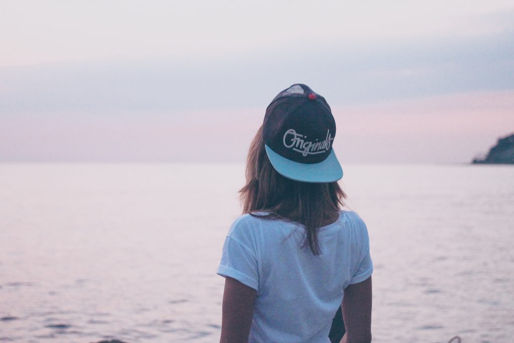 a girl wearing a backwards baseball cap gazes out toward the ocean