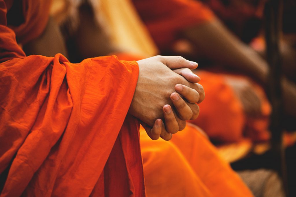 person in orange robe with fingers entwined