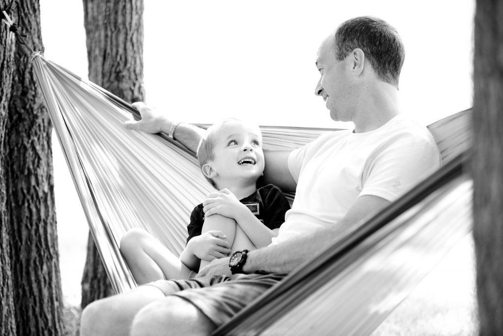 father and young son sit on a hammock
