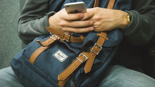 man sitting with a backpack on lap using cell phone