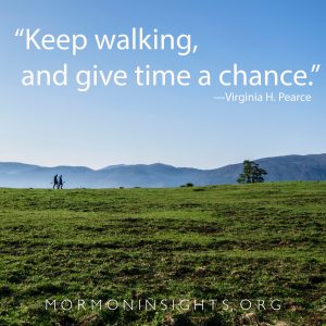 "Keep walking and give time a chance." -Virginia H. Pearce. Grassy field with two people walking with mountains in the background.