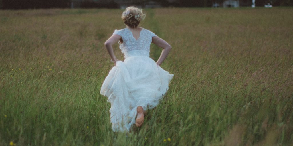 Woman in wedding dress running away in a field
