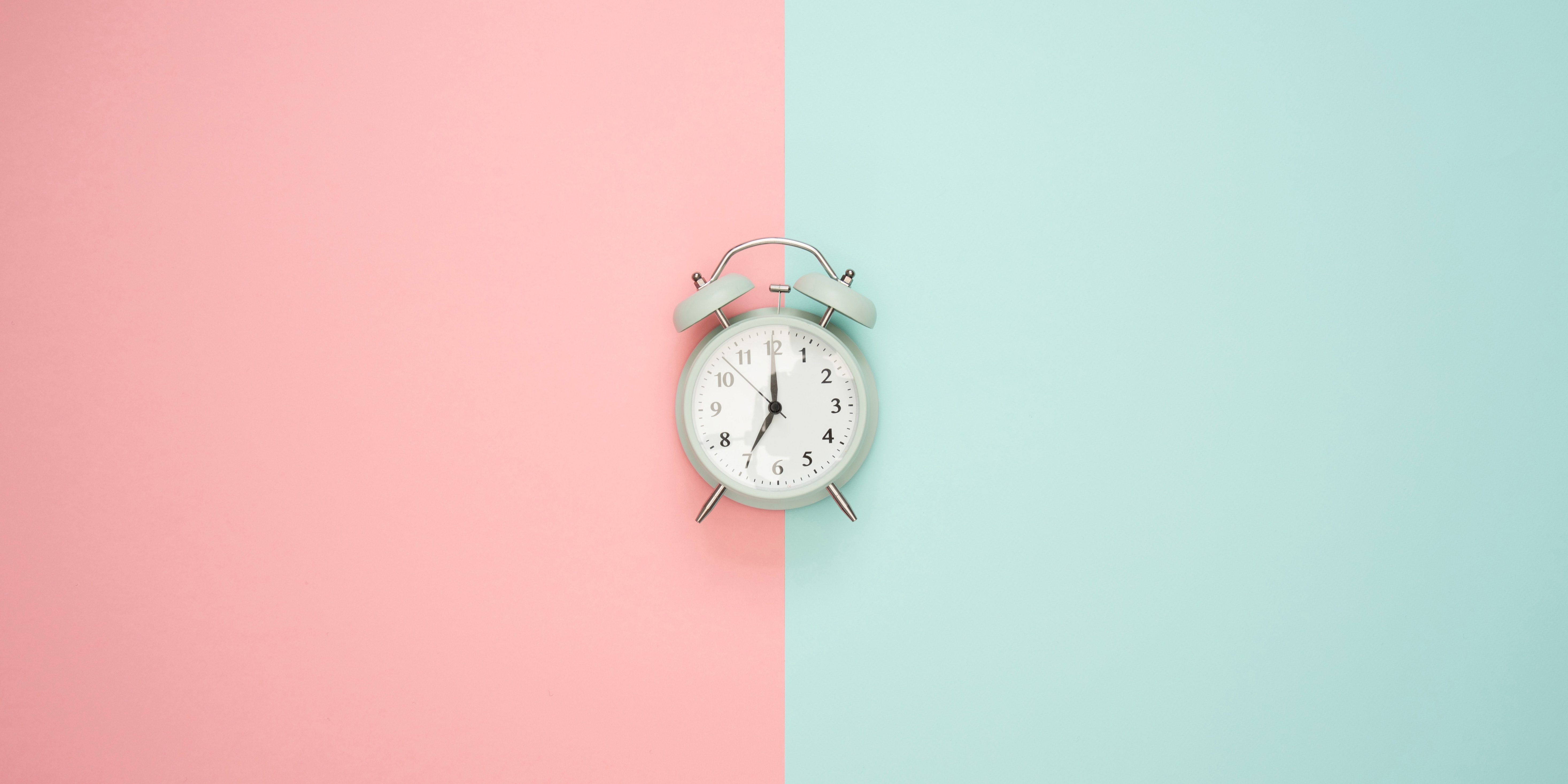 Alarm clock on pink and mint green background