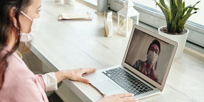 A photograph of a woman video chatting with a man; both are wearing cloth masks