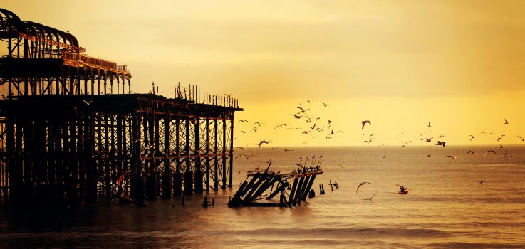 Old pier at sunset with flying seagulls.