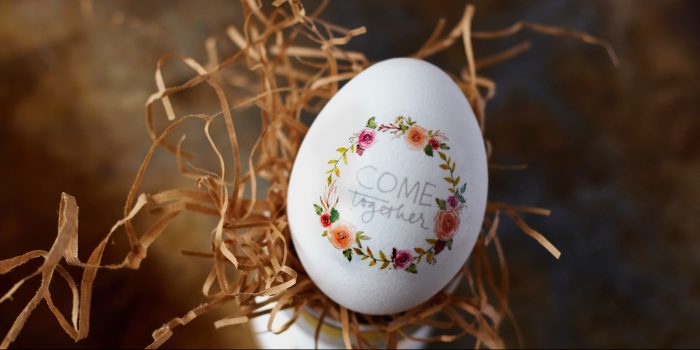 An egg with the words "Come Together" and a wreath of flowers painted on it.
