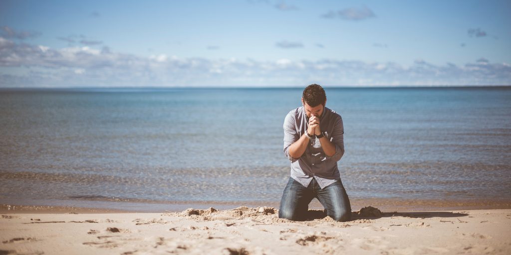 Man kneeling on a beach in fervent prayer