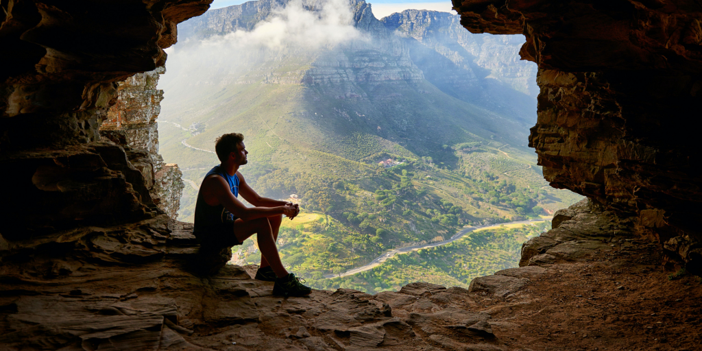 Man silhouetted against the mouth of a cave over a scenic overlook