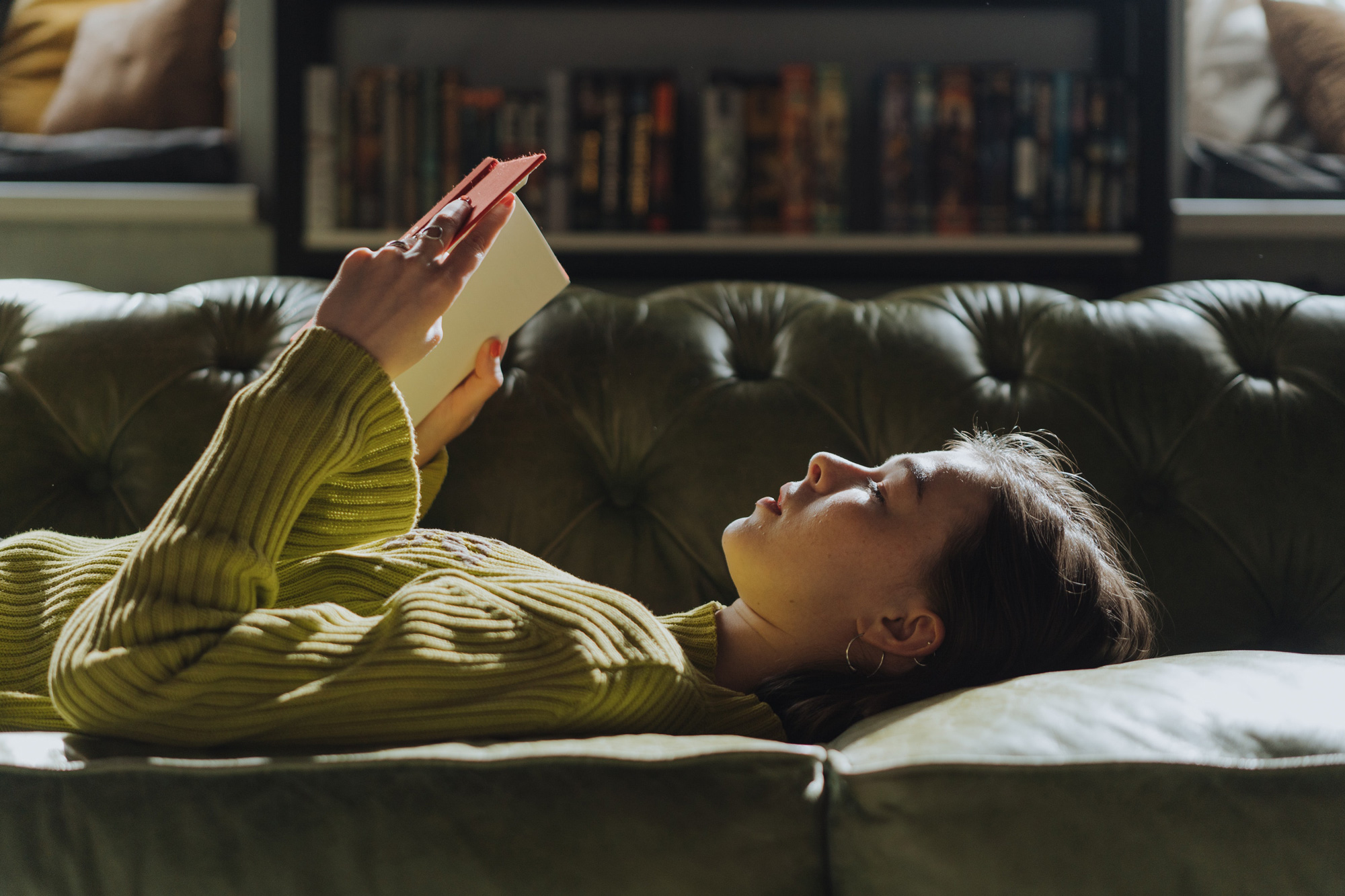 Woman in Yellow Long Sleeve Shirt Lying on her back on a Couch reading