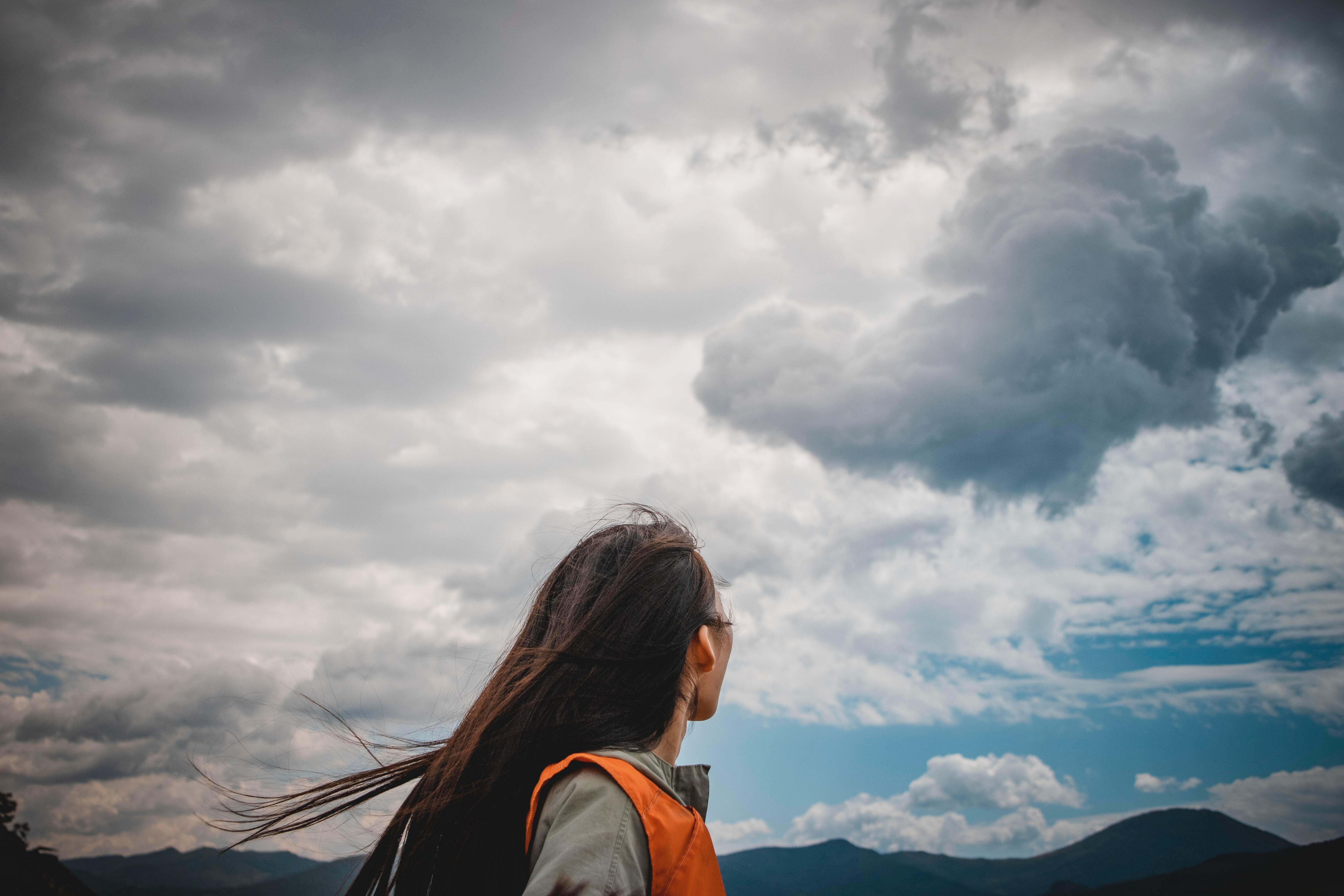 Woman in an orange vest looking at a cloudy sky.