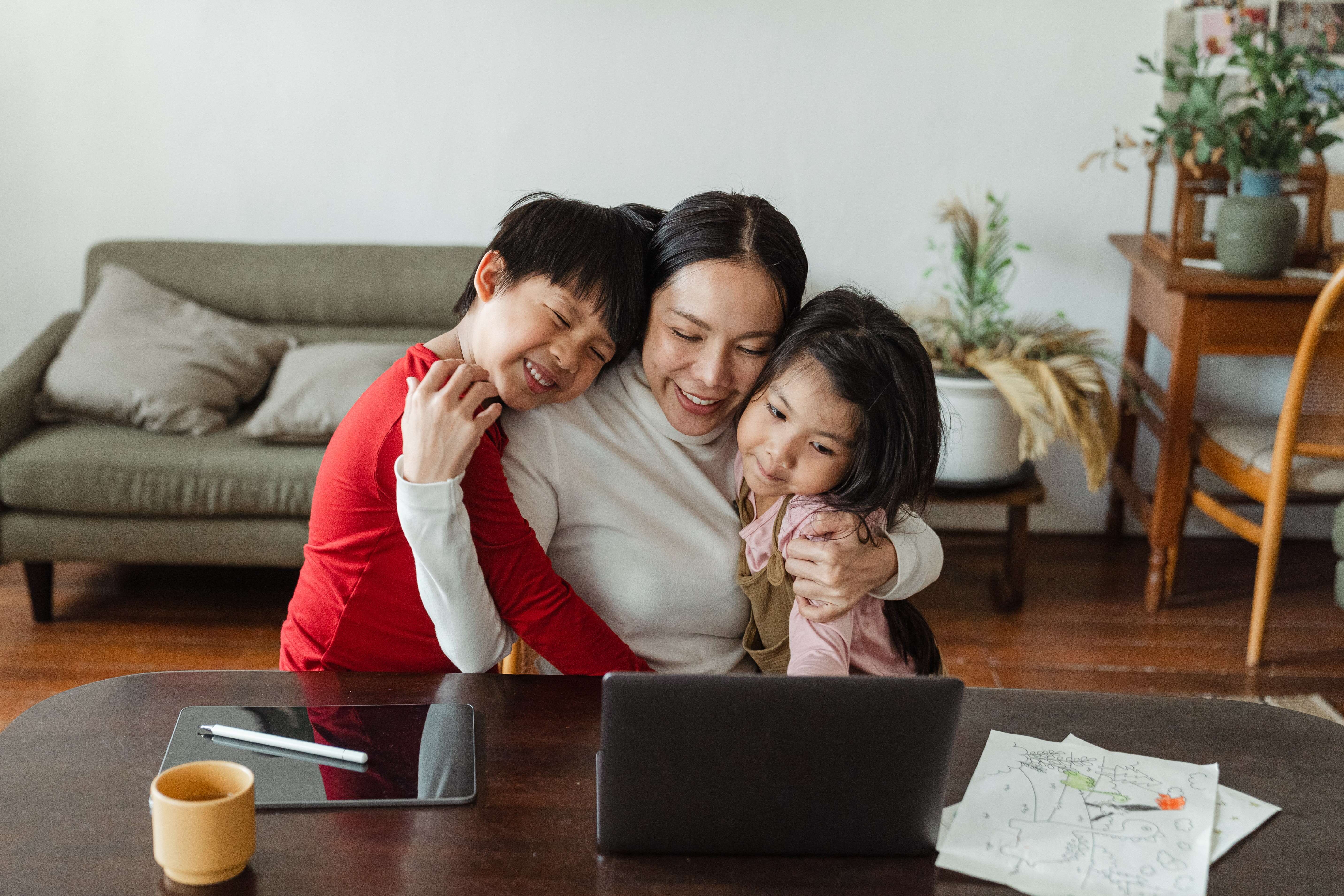 Woman being embraced by her children while sitting in front of her laptop.