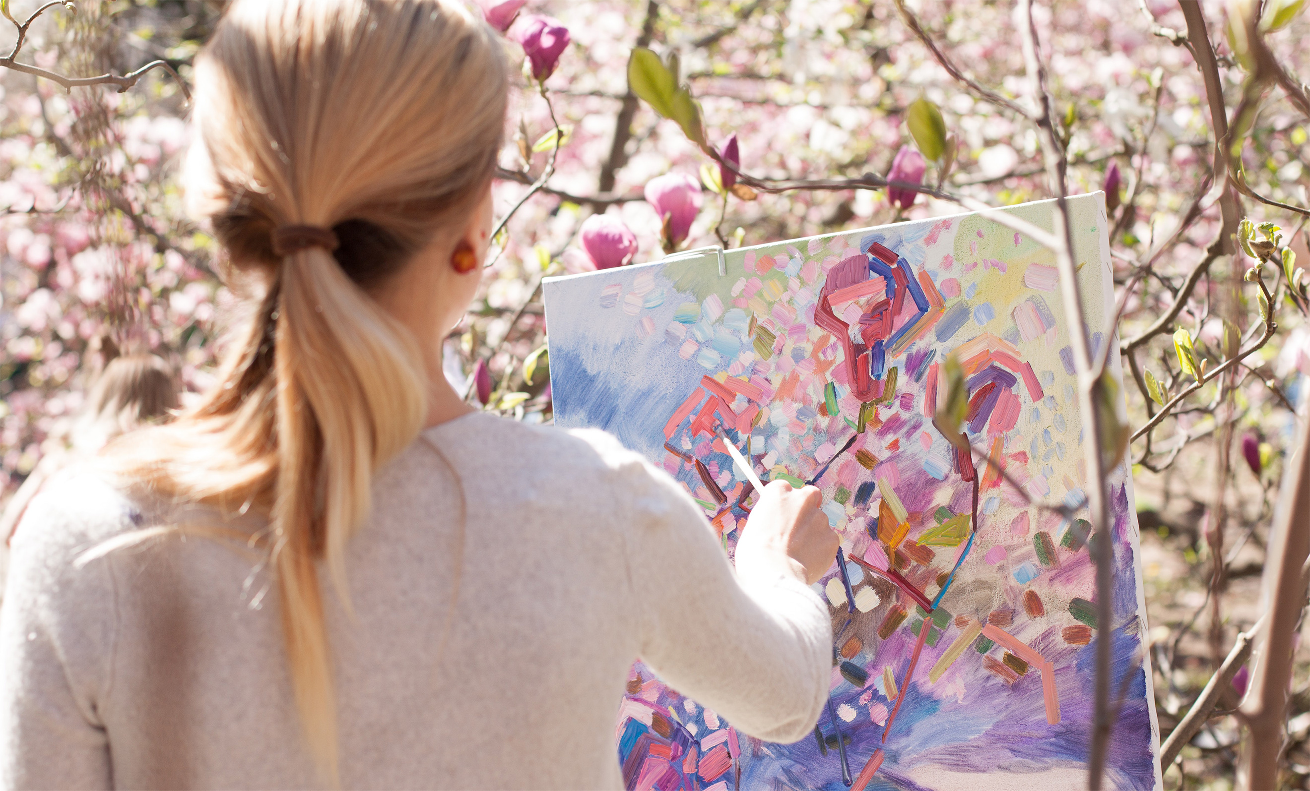 Woman painting pink flowers on canvas outside
