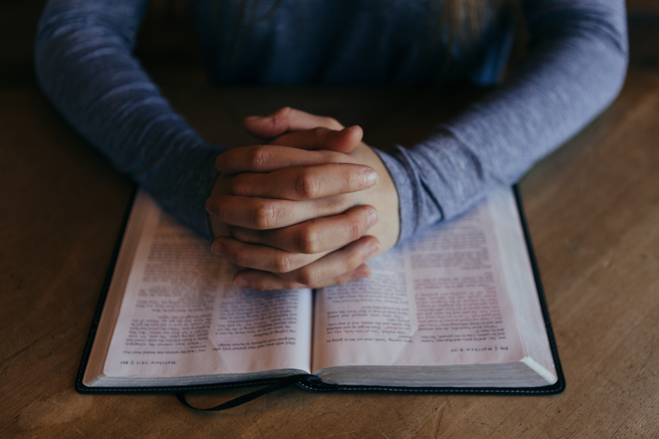 folded hands over an open Bible