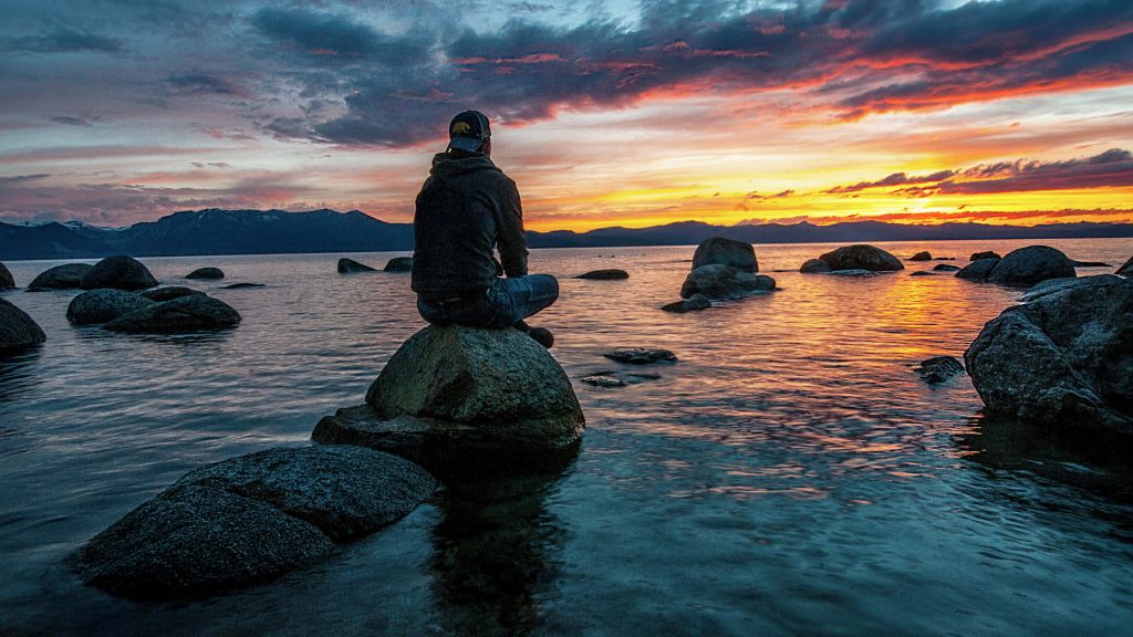 A man sitting on a rock in a lake, looking at a sunset