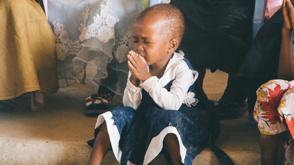 A child in a dress sits in prayer