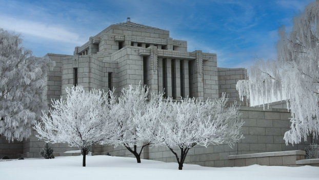 The Cardston Alberta Temple during winter, a white granite building with snow covered grounds and frost covered trees surrounding it.