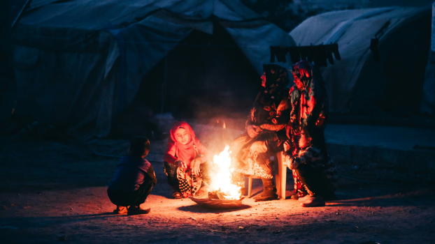 A group of people sitting around a bright fire in a refugee camp.