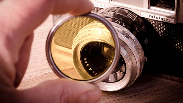 A yellow-tinted camera lens/filter is held in front of a camera.